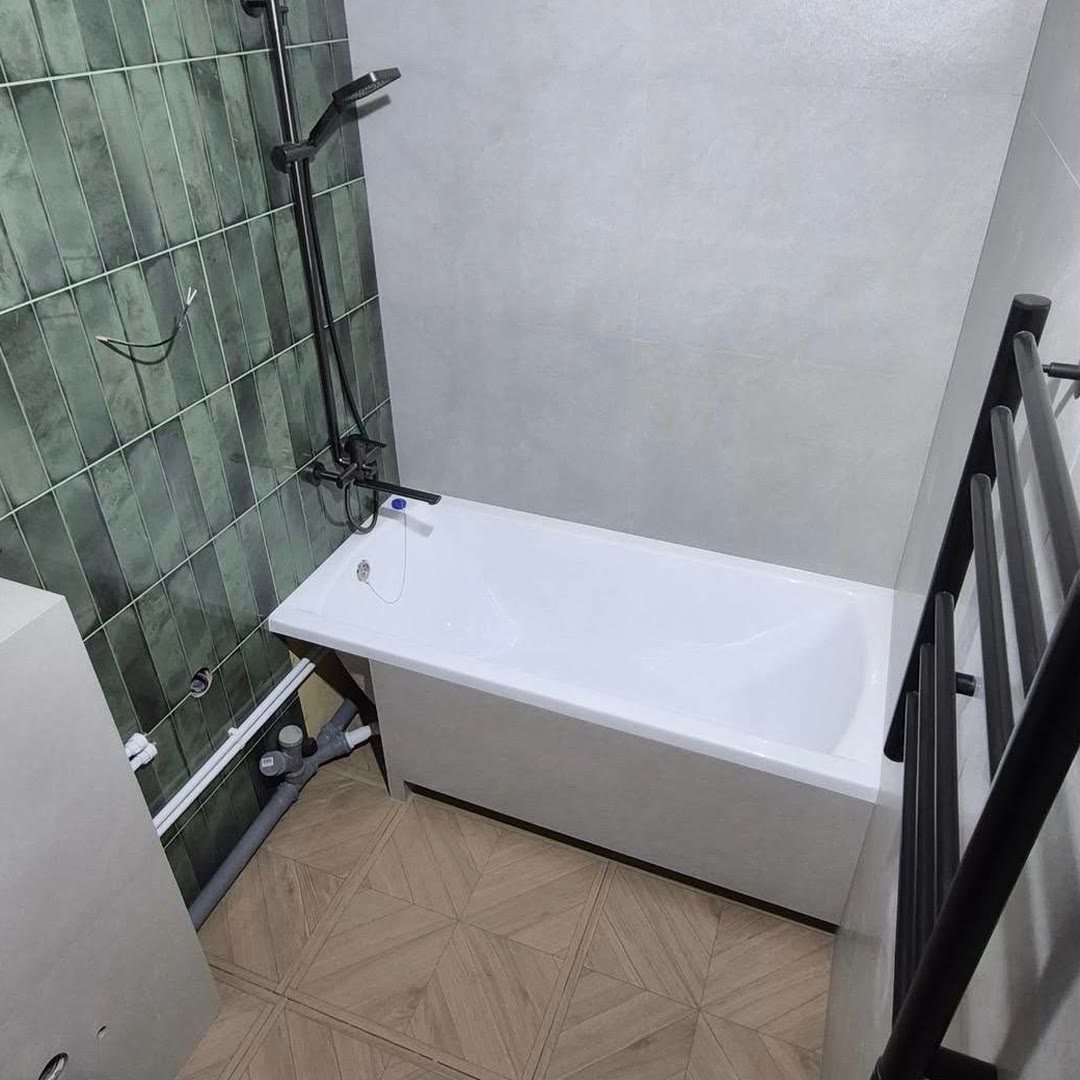 Finished bathroom with a green tiled feature wall, concrete-effect tiling, black shower riser and a parquet-pattern tiled floor