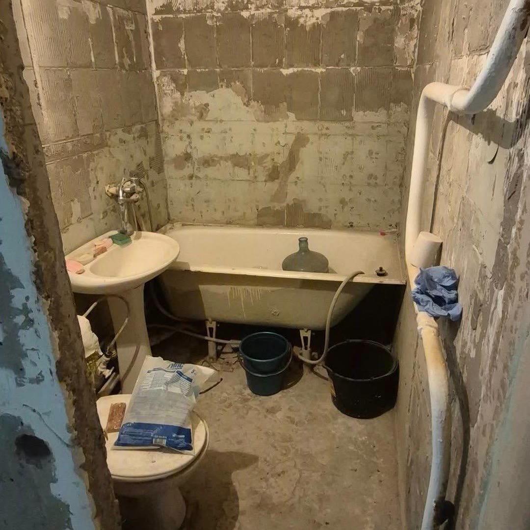 Small bathroom stripped back to bare walls, old bath and basin still in place