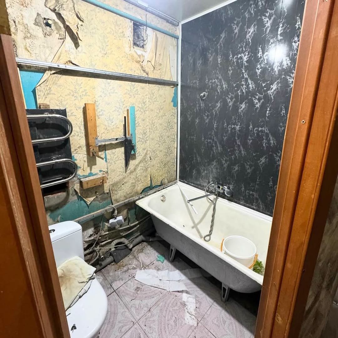 Derelict bathroom with torn wallpaper, exposed pipework and an old enamel bath