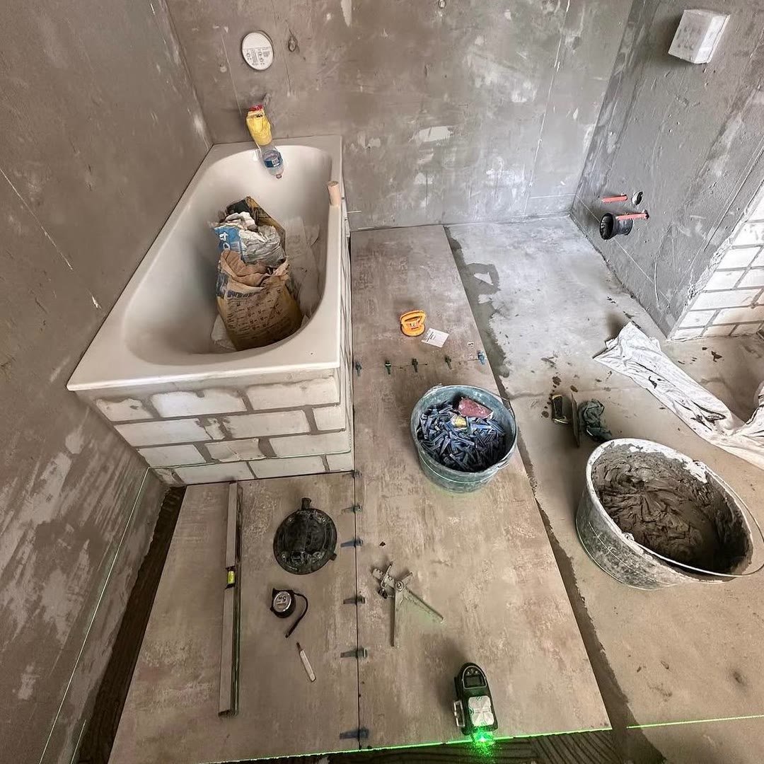Bathroom floor being tiled, with a laser level projecting a line, tile levelling clips and adhesive mixed in a bucket