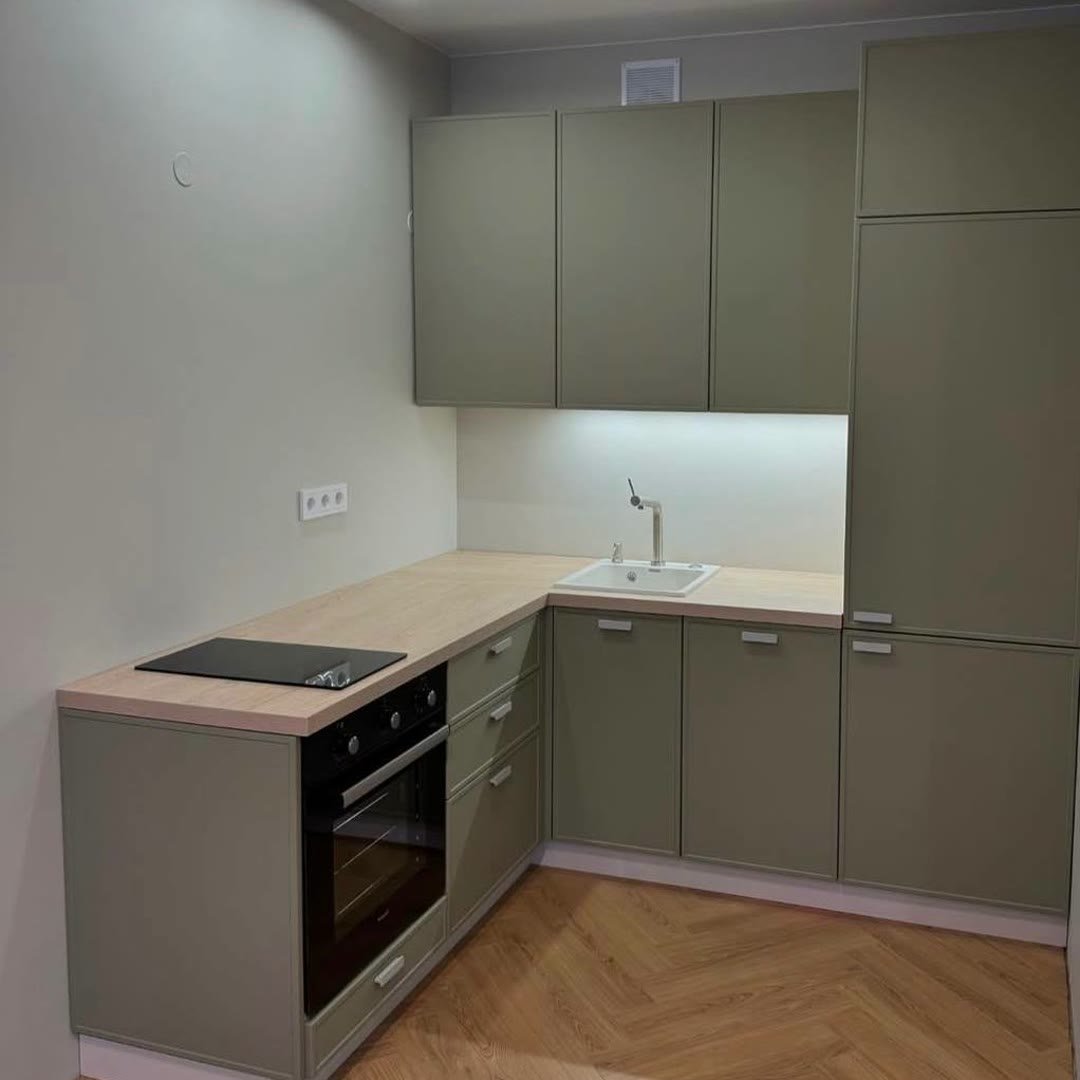 Fitted L-shaped kitchen with sage-green units, wood worktop, built-in oven and hob, under-cabinet lighting