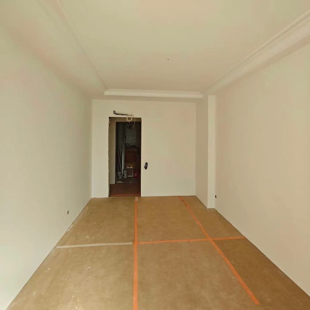 Long room freshly painted in off-white, floor covered in protective paper taped at the joins