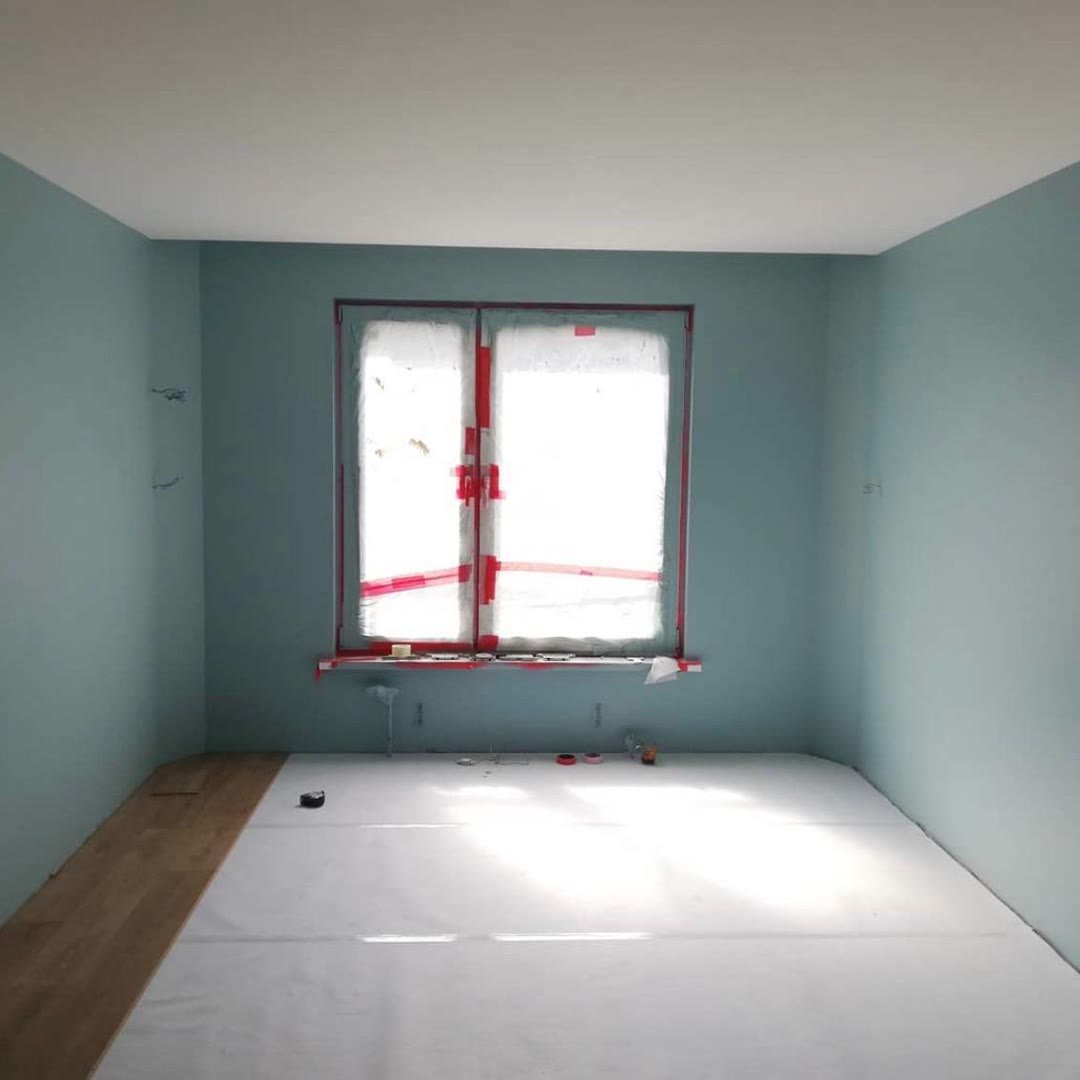 Bedroom painted pale green, window frame masked with red tape, floor covered in white protection