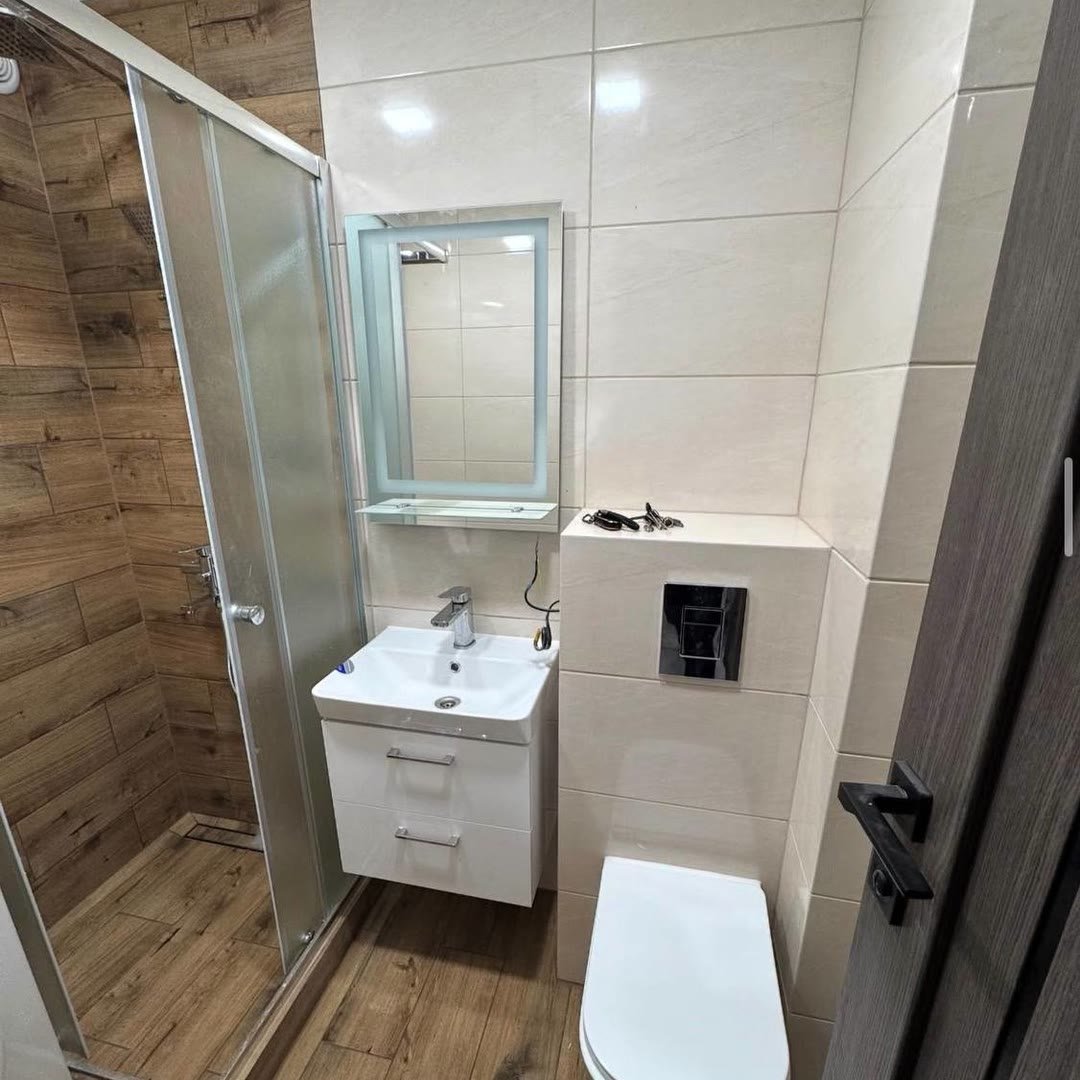 Finished shower room with a wall-hung WC, vanity unit, lit mirror and wood-effect floor tiling