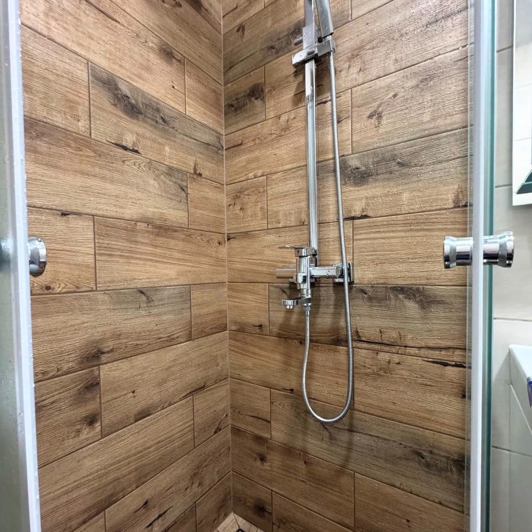 Shower enclosure tiled in wood-effect tiles with a chrome shower riser fitted