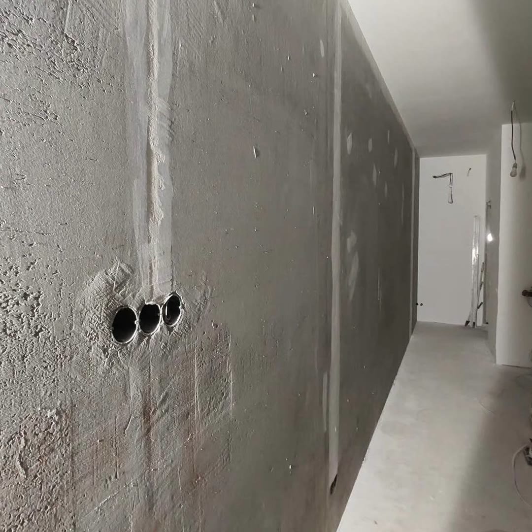 Long concrete wall with filler patched over it, three socket holes cut low down, before skimming
