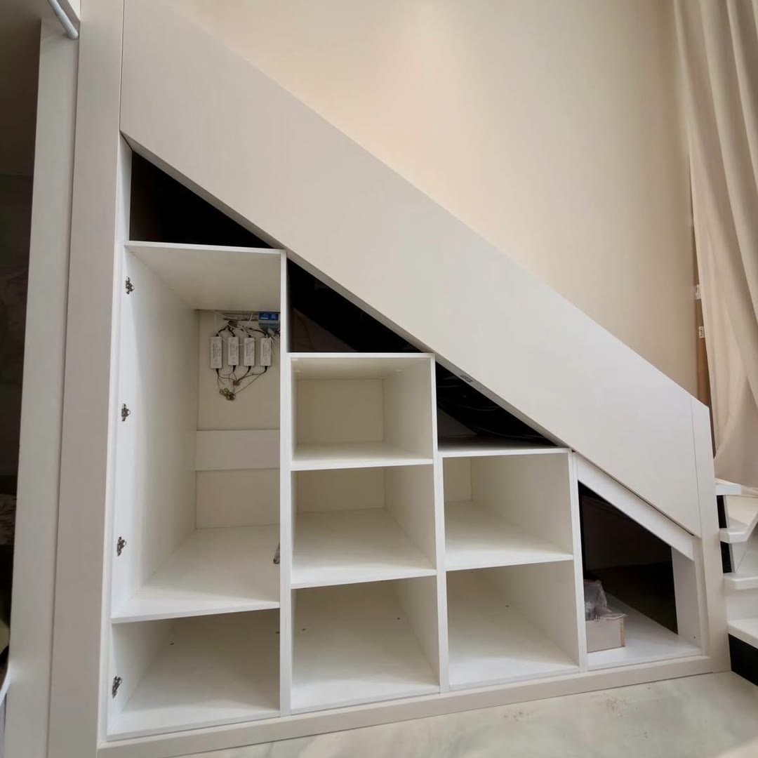 White fitted storage built into the space under a staircase, open shelves stepping down with the stairs